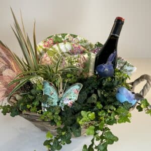 cesta de mimbre campestre con plantas verdes, platos servilletas, una botella de vino y adornos variados.
