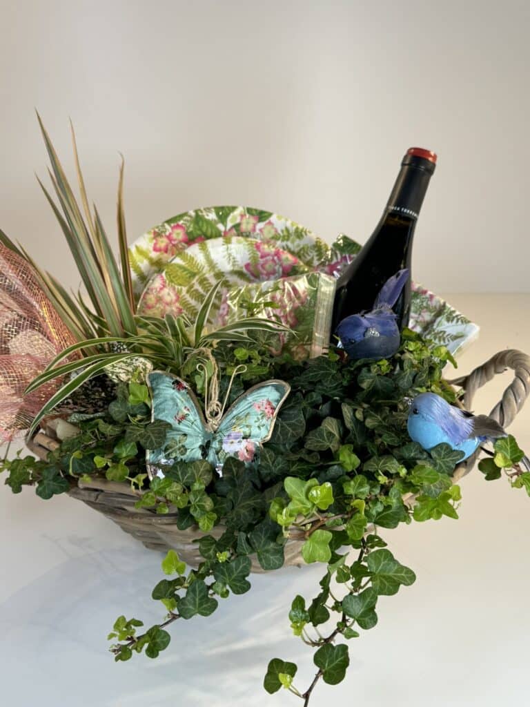 cesta de mimbre campestre con plantas verdes, platos servilletas, una botella de vino y adornos variados.