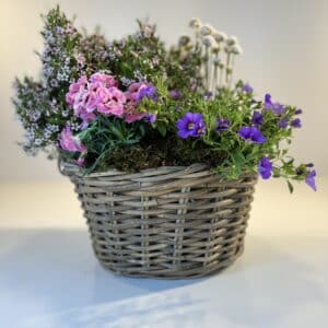 cesta de mimbre con flores silvestres en rosa, blanco y morado.