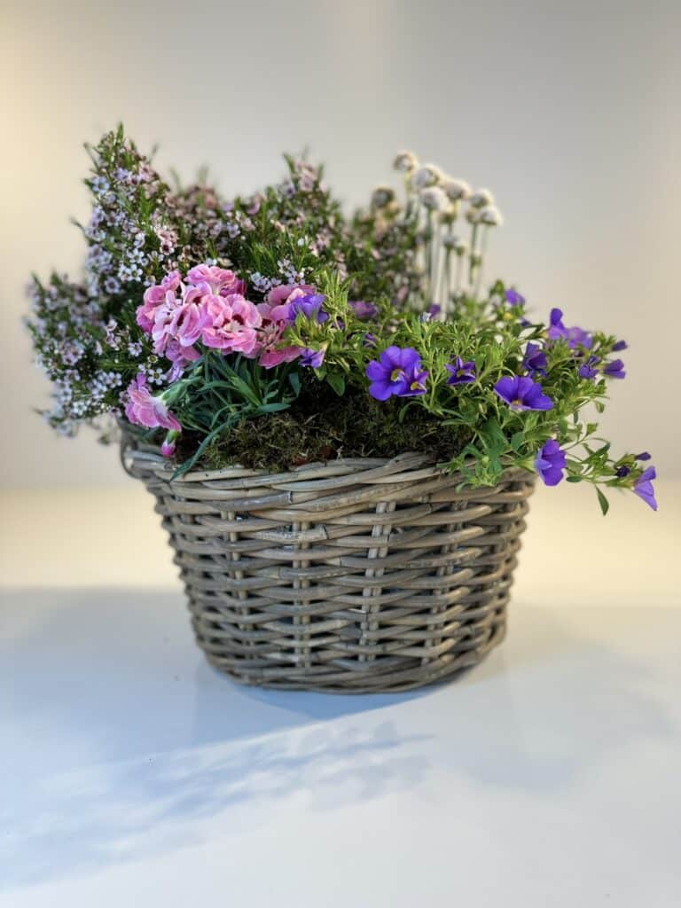 cesta de mimbre con flores silvestres en rosa, blanco y morado.