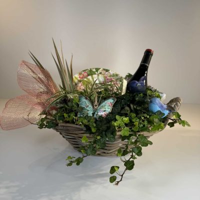 cesta de mimbre campestre con plantas verdes, platos servilletas, una botella de vino y adornos variados.